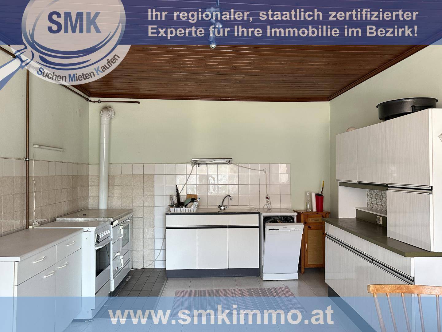 Funktionale Küche mit weißen Schränken, Spüle und älteren Geräten.