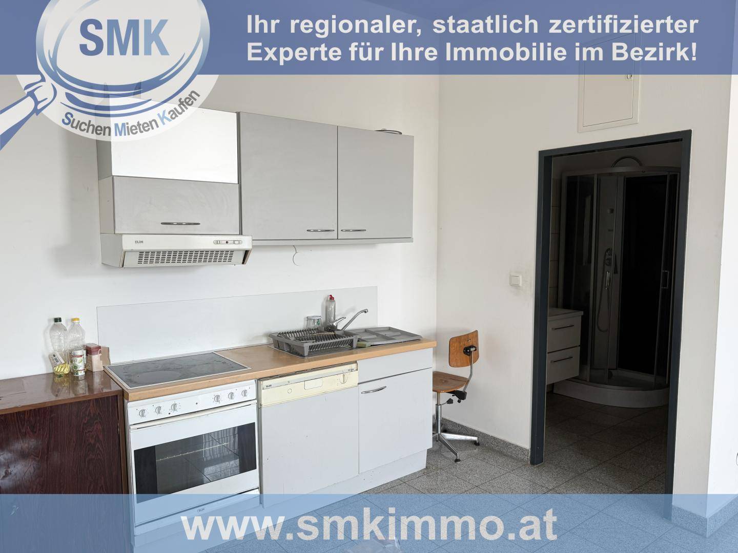 Funktionale Küche mit grauen Schränken, Elektroherd, Spüle und Geschirrspüler, angrenzend an ein Badezimmer.
