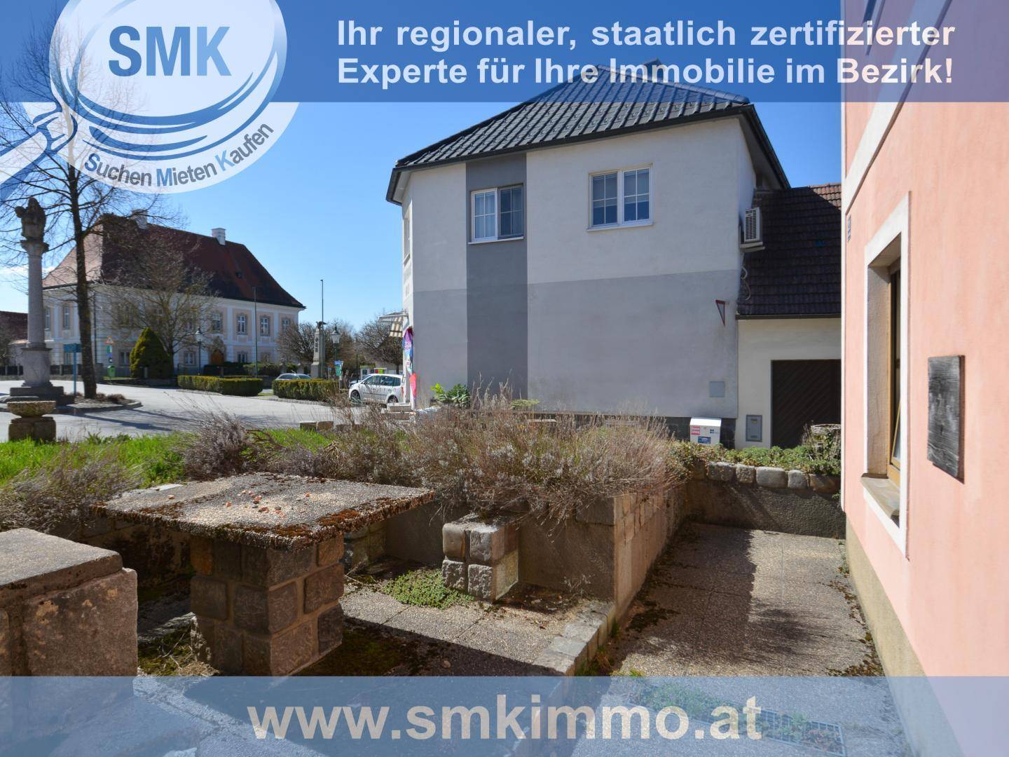 Ansicht eines Gebäudes mit grauer und weißer Fassade an einem öffentlichen Platz mit Denkmal.