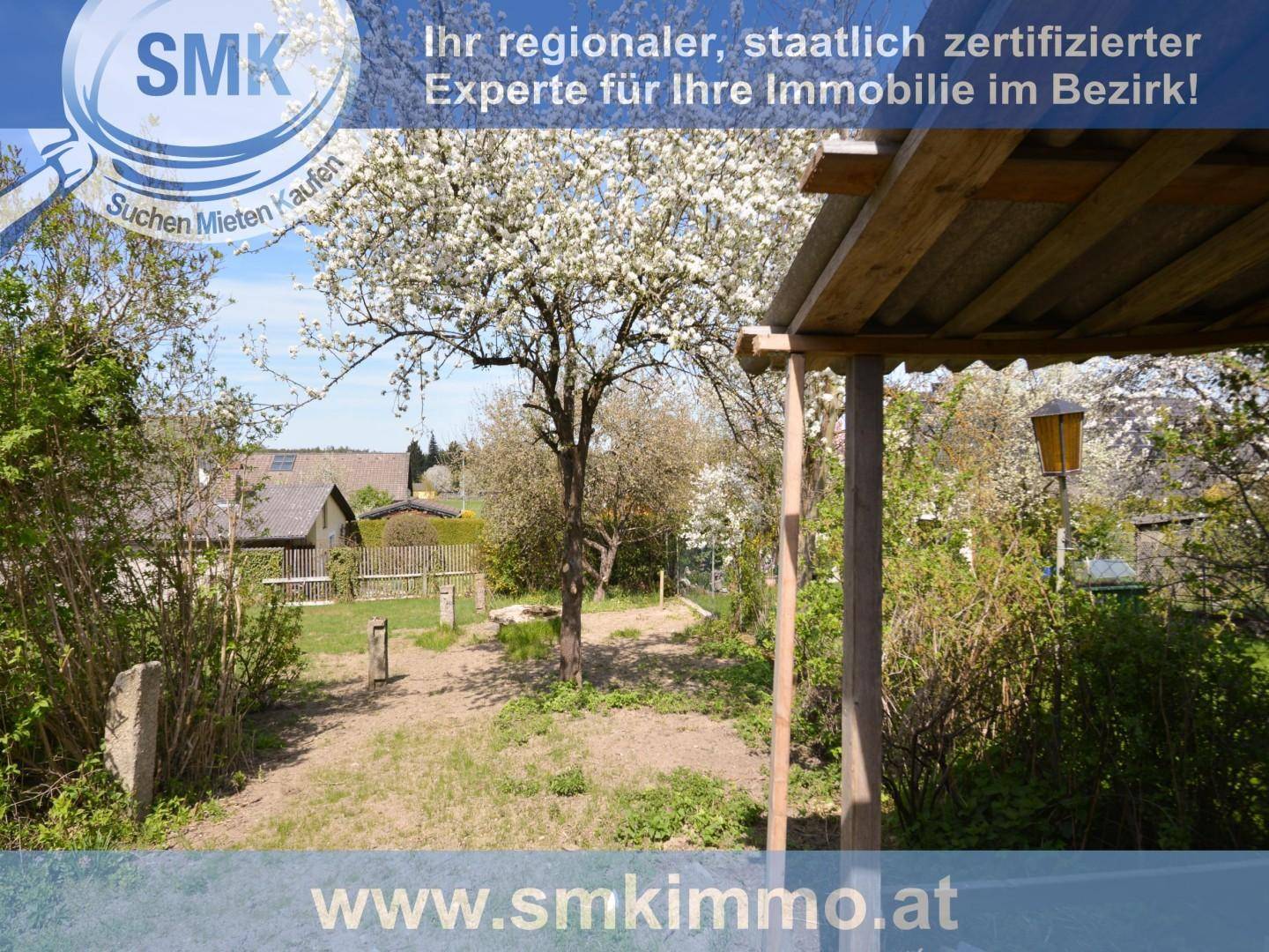 Gartenbereich mit blühenden Bäumen und einem Holzunterstand, umgeben von viel Grün.