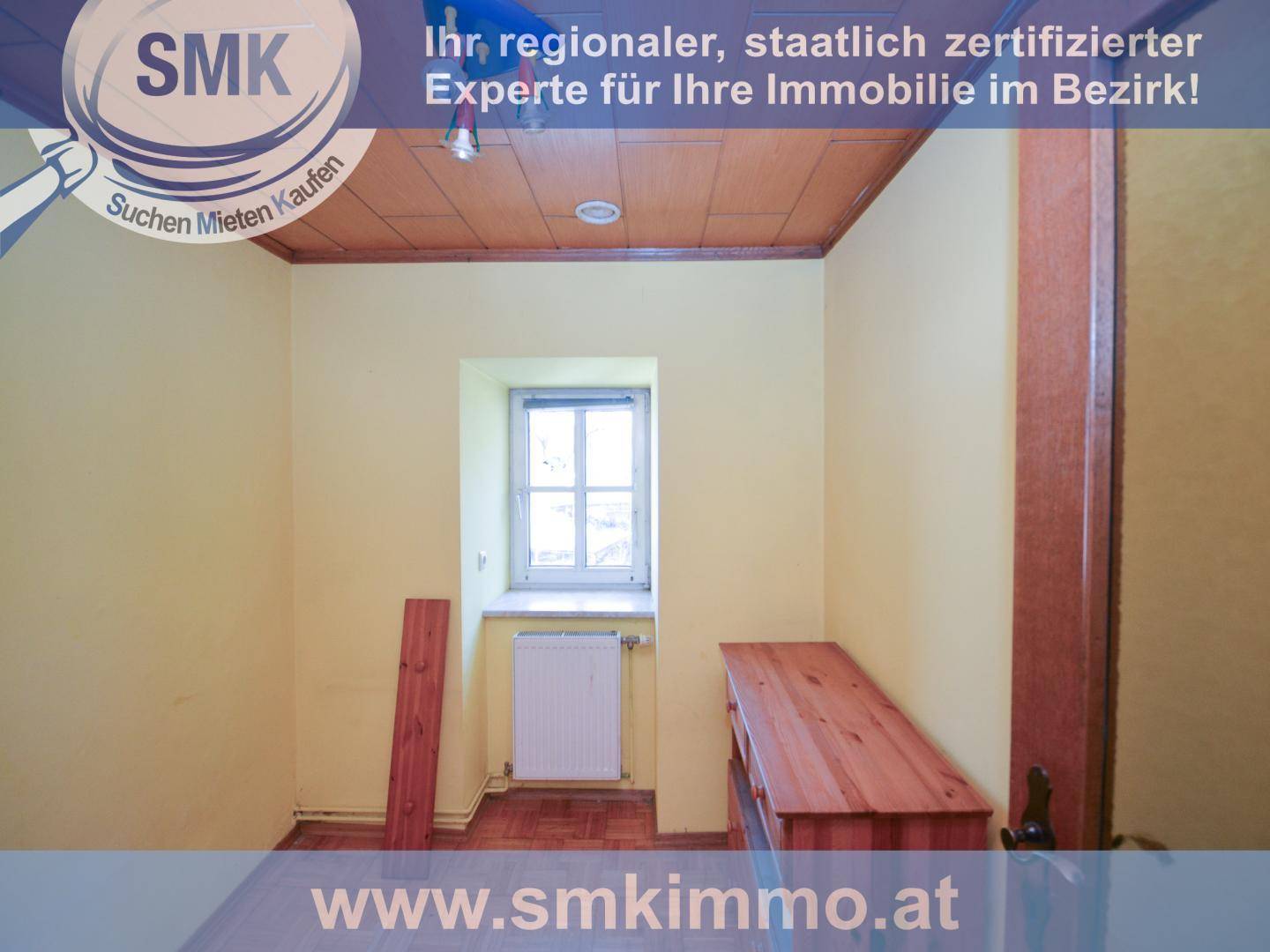 Kleines Zimmer mit gelben Wänden, Holzdeckenverkleidung und einem Fenster mit Heizkörper.