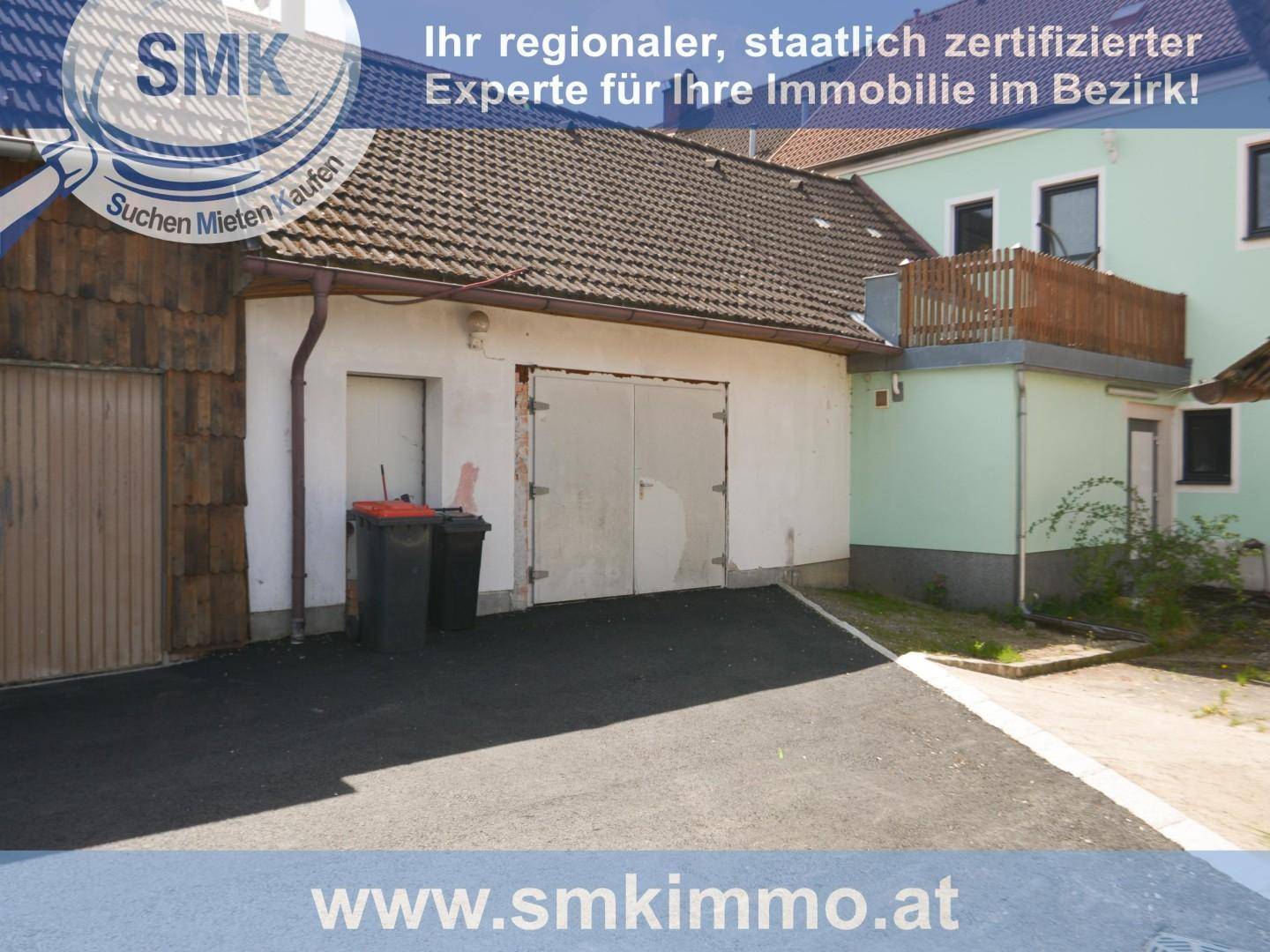 Außenansicht eines Gebäudes mit Garagentoren und einem Balkon im oberen Bereich.
