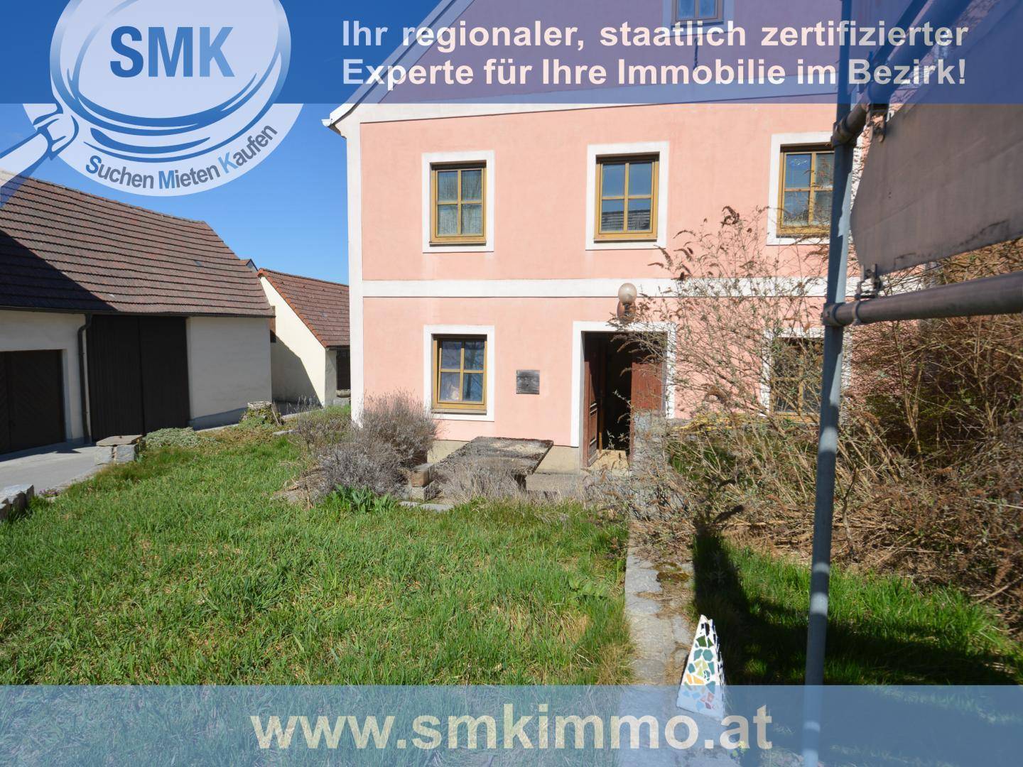 Seitenansicht des rosa Hauses mit ungepflegtem Gartenbereich und Nebengebäuden im Hintergrund.