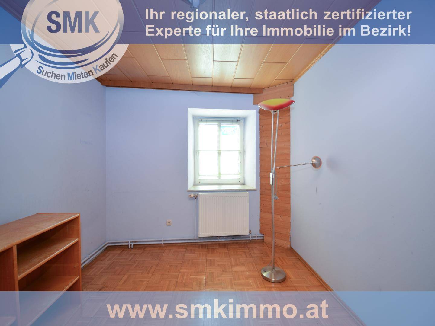 Zimmer mit Holzdeckenverkleidung, Parkettboden und einer Stehlampe neben dem Fenster.