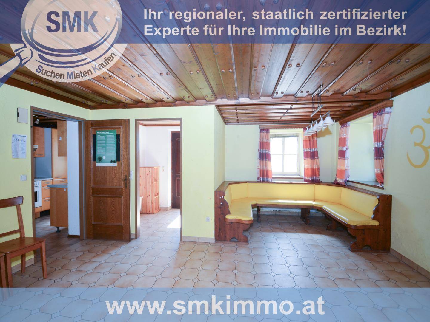 Rustikaler Wohnbereich mit Holzbalkendecke, Fliesenboden und einer Eckbank am Fenster.