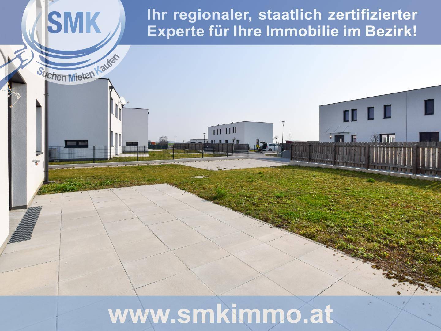 Gepflasterte Terrasse und Rasenfläche mit Blick auf weitere moderne Neubauten.