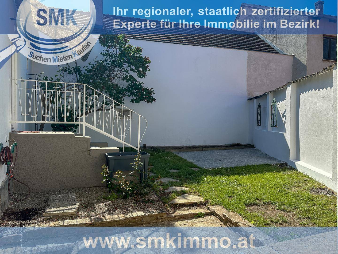 Kleiner Gartenbereich mit Treppe zum Hauseingang und weißer Fassade.