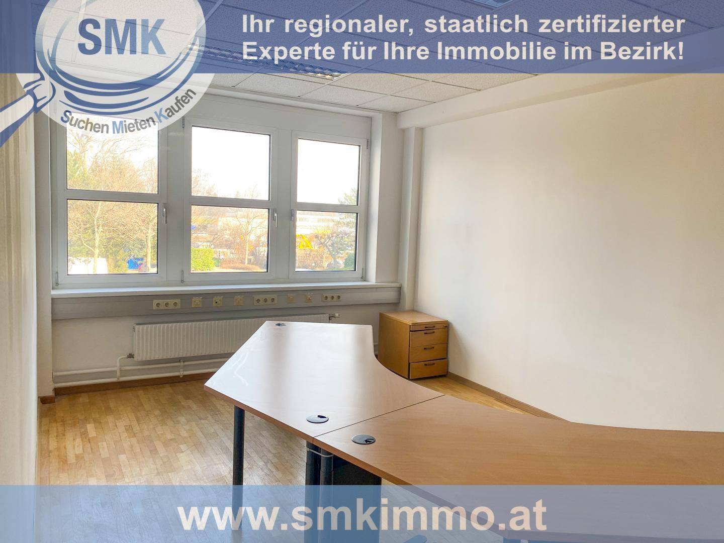 Helles Eckbüro mit einem großen Schreibtisch, Rollcontainer und Fenstern mit Blick ins Grüne.