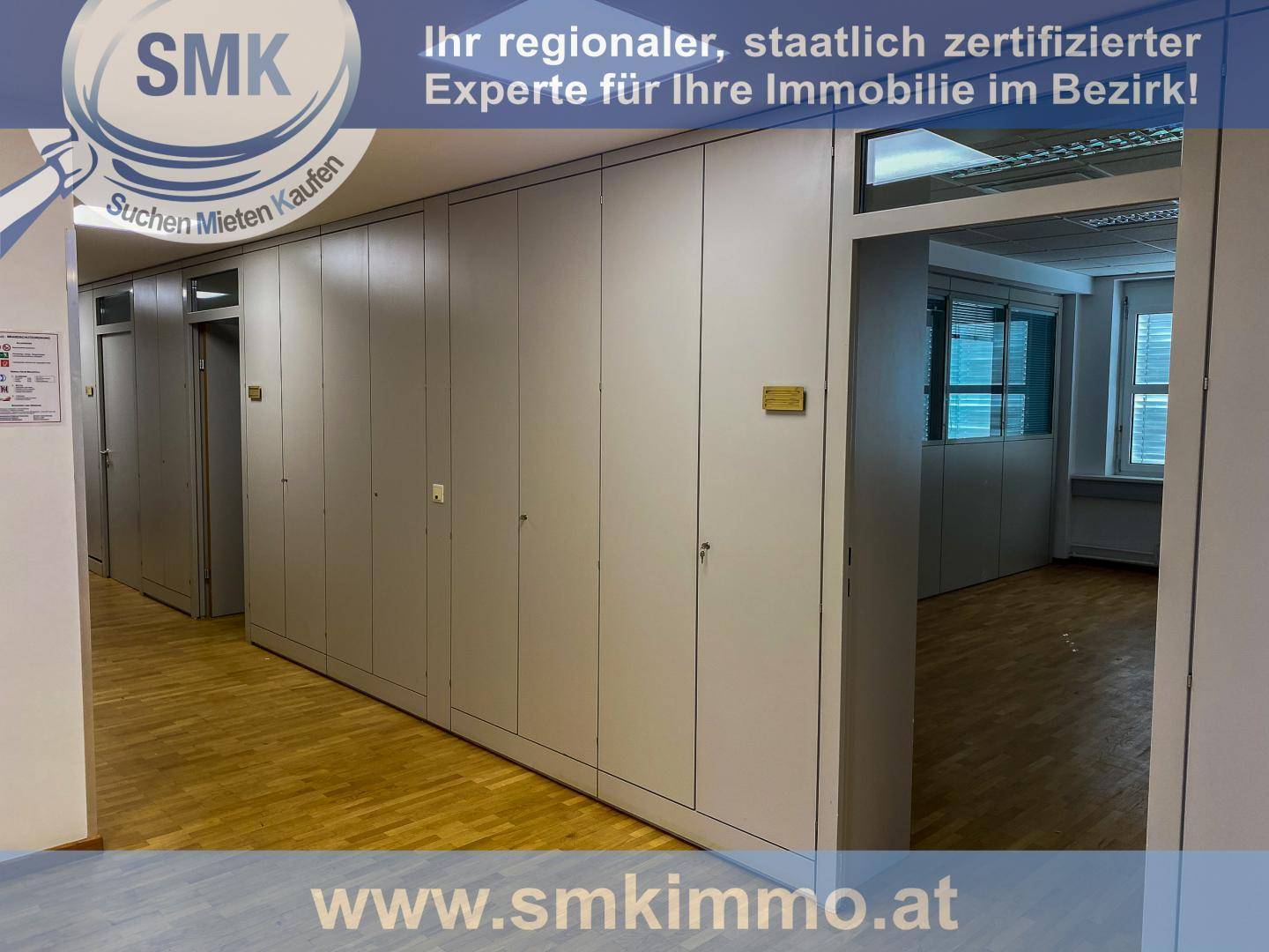 Langer Flur mit vielen grauen Einbauschränken und Holzfußboden, der zu weiteren Büroräumen führt.