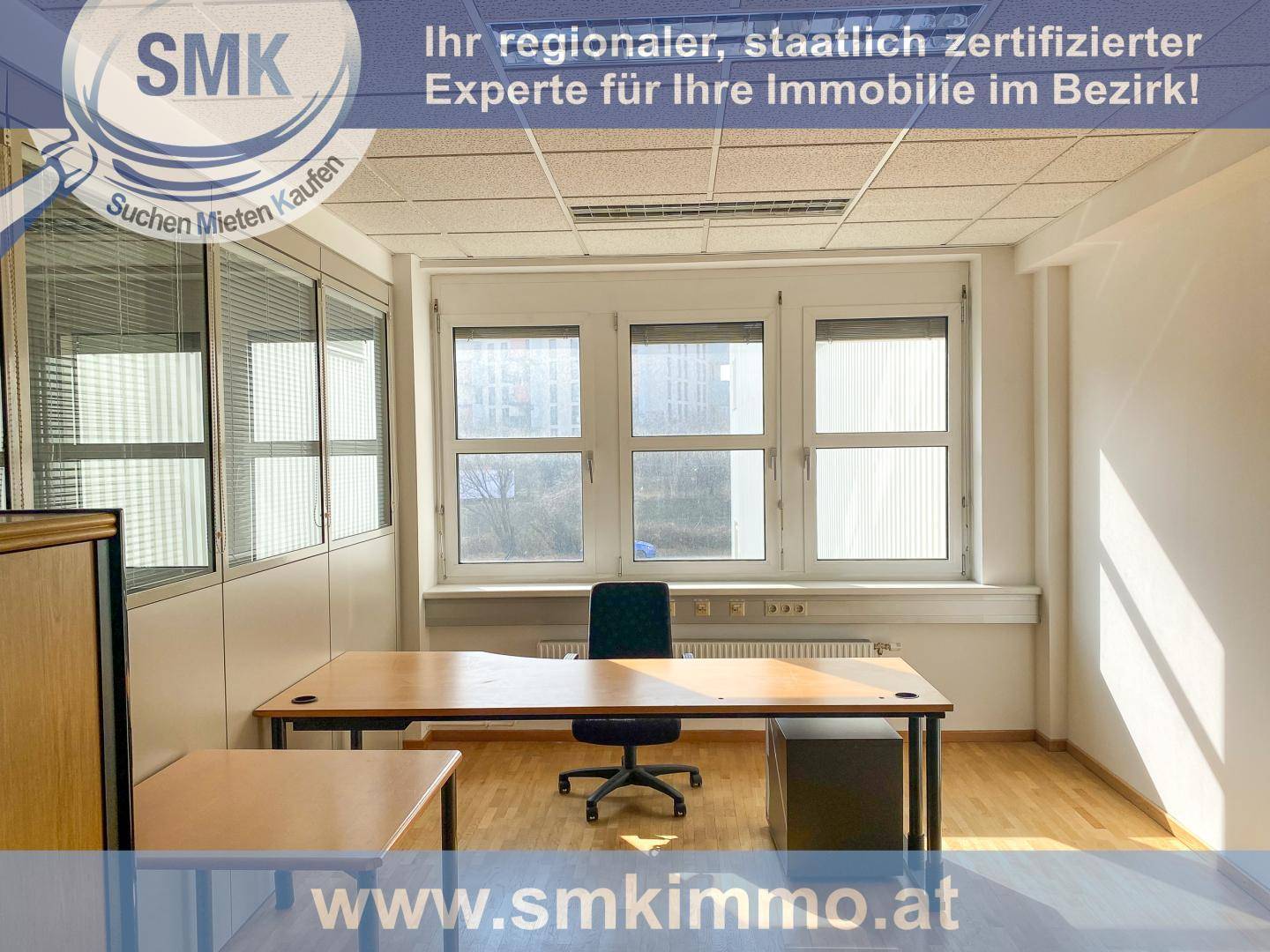 Helles Büro mit einem Schreibtisch, Bürostuhl und großen Fenstern, die viel Tageslicht hereinlassen.