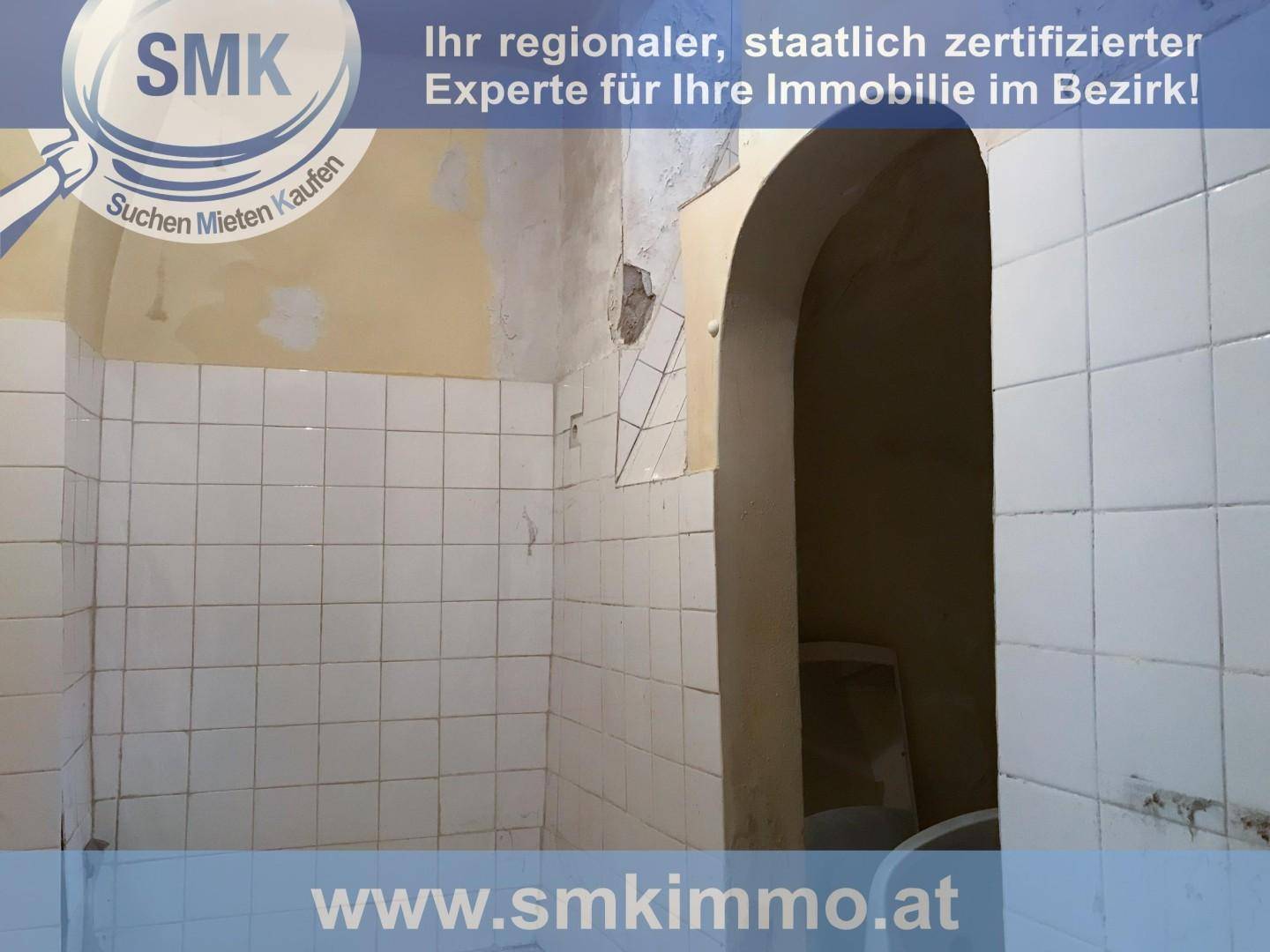 Badezimmer im Rohzustand mit alten weißen Fliesen und einem gemauerten Bogen.