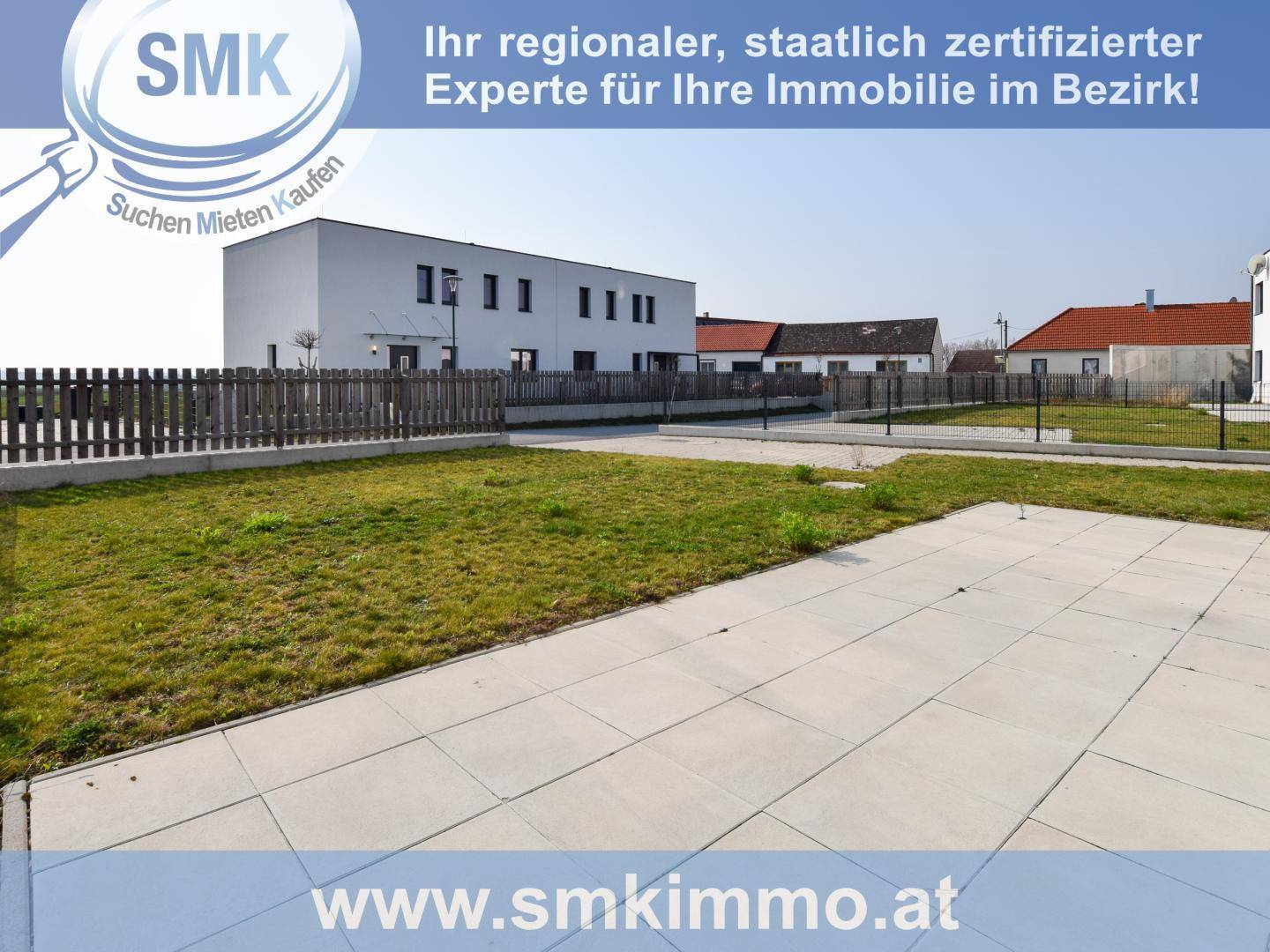 Außenansicht eines Neubaus mit gepflasterter Terrasse und Rasenfläche im Vordergrund.