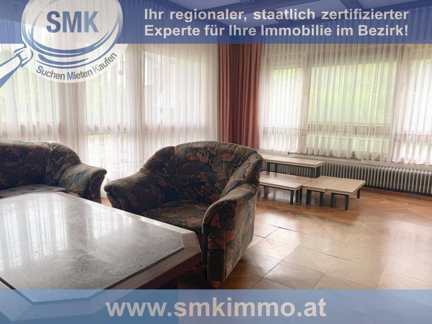 Helles Wohnzimmer mit großen Fenstern, gemusterten Sesseln und Parkettboden.