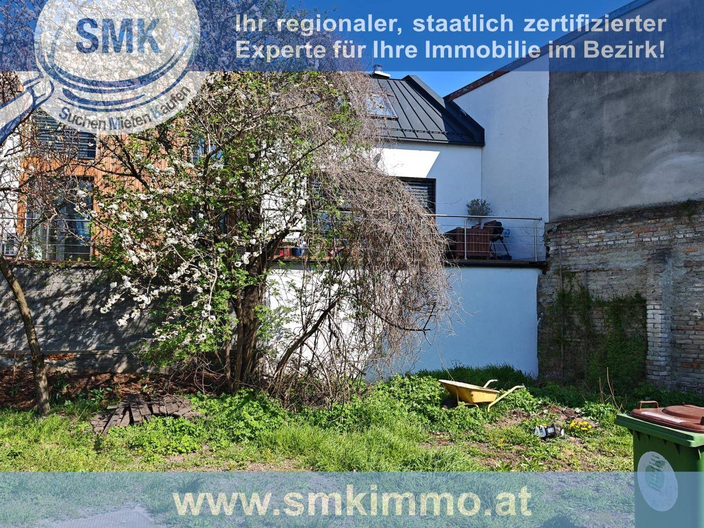 Garten mit blühendem Baum, Rasen und Blick auf einen Balkon des Nachbargebäudes.