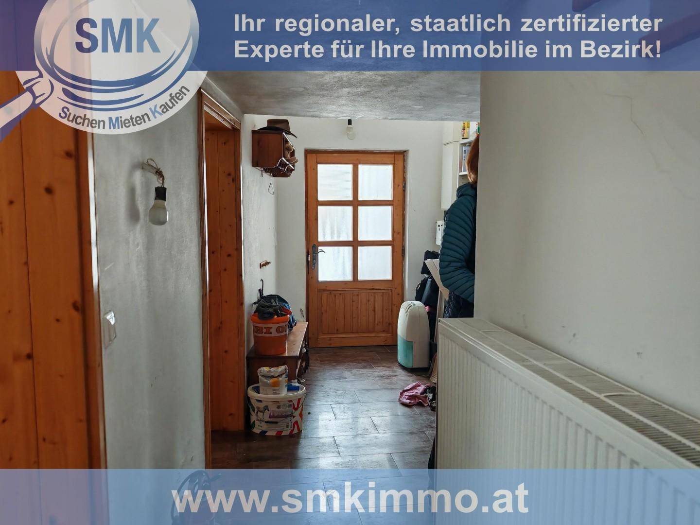 Eingangsbereich mit Holztür, Heizkörper und einfacher Einrichtung, die auf einen Flur führt.