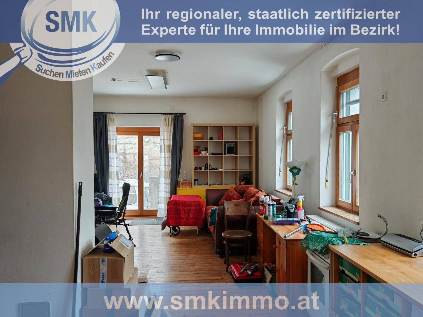 Unaufgeräumter Wohnbereich mit Holzboden, vielen Fenstern und Zugang zu einem Außenbereich.