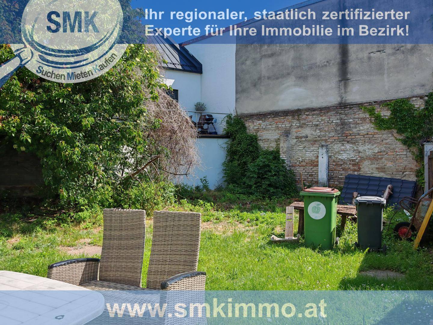 Gartenbereich mit Sitzgelegenheiten, einer alten Ziegelwand und Mülltonnen im Hintergrund.