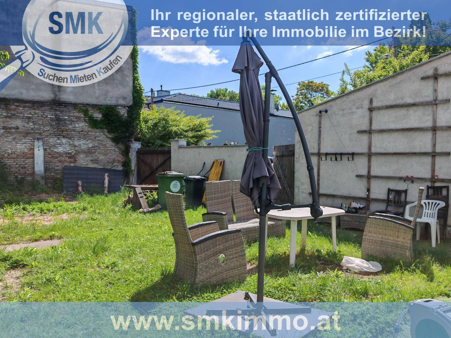 Gartenbereich mit Outdoor-Sitzgruppe, Sonnenschirm und Blick auf eine alte Gebäudewand.