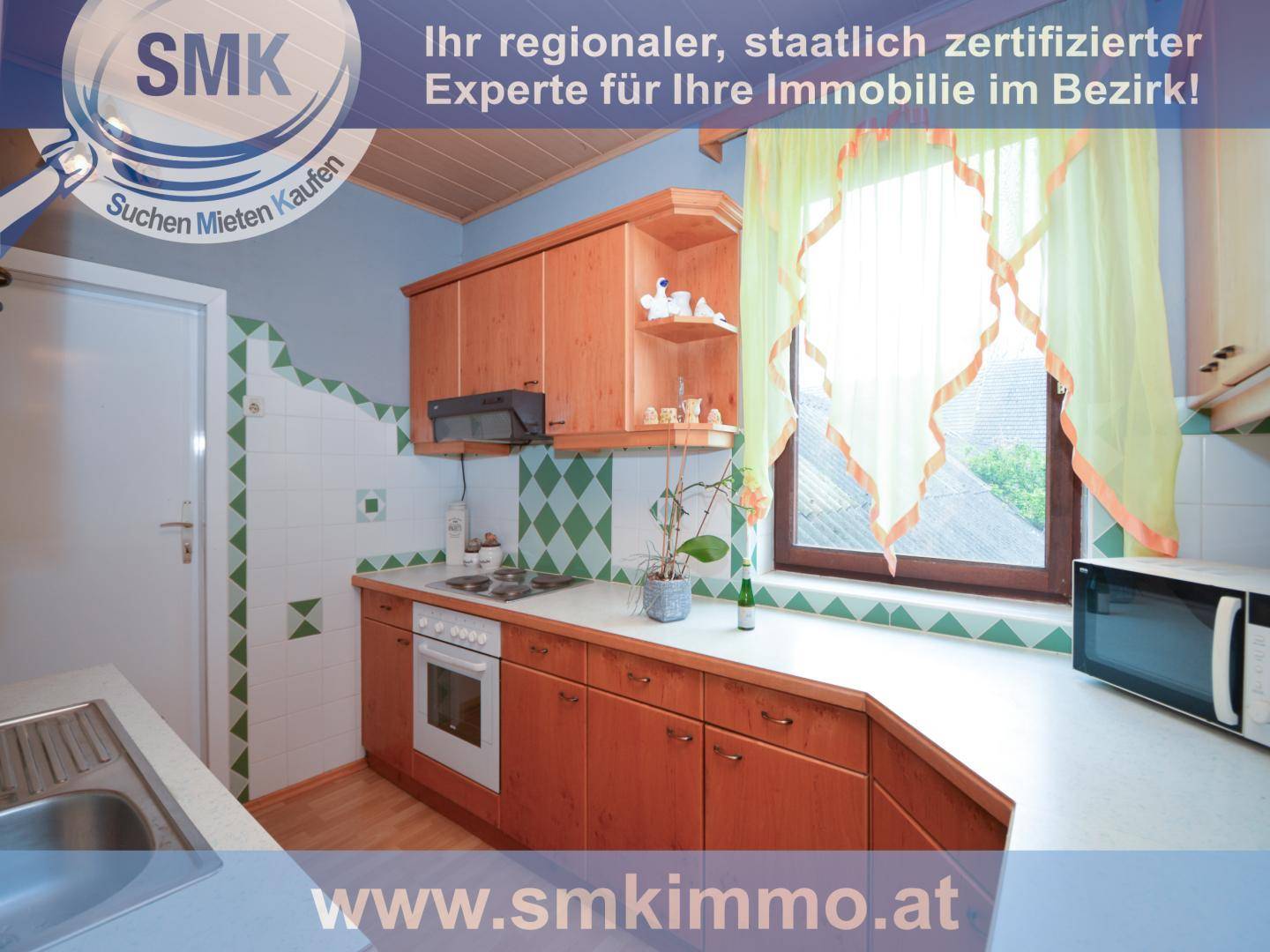 Funktionale Küche mit Holzschränken, Arbeitsplatte und Fenster mit Blick ins Grüne.