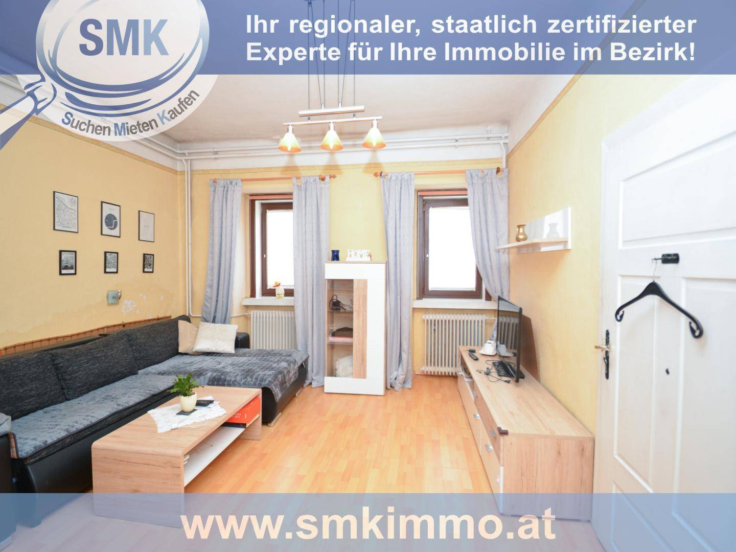 Gemütliches Wohnzimmer mit Sofa, Holzboden und zwei Fenstern, die viel Licht hereinlassen.