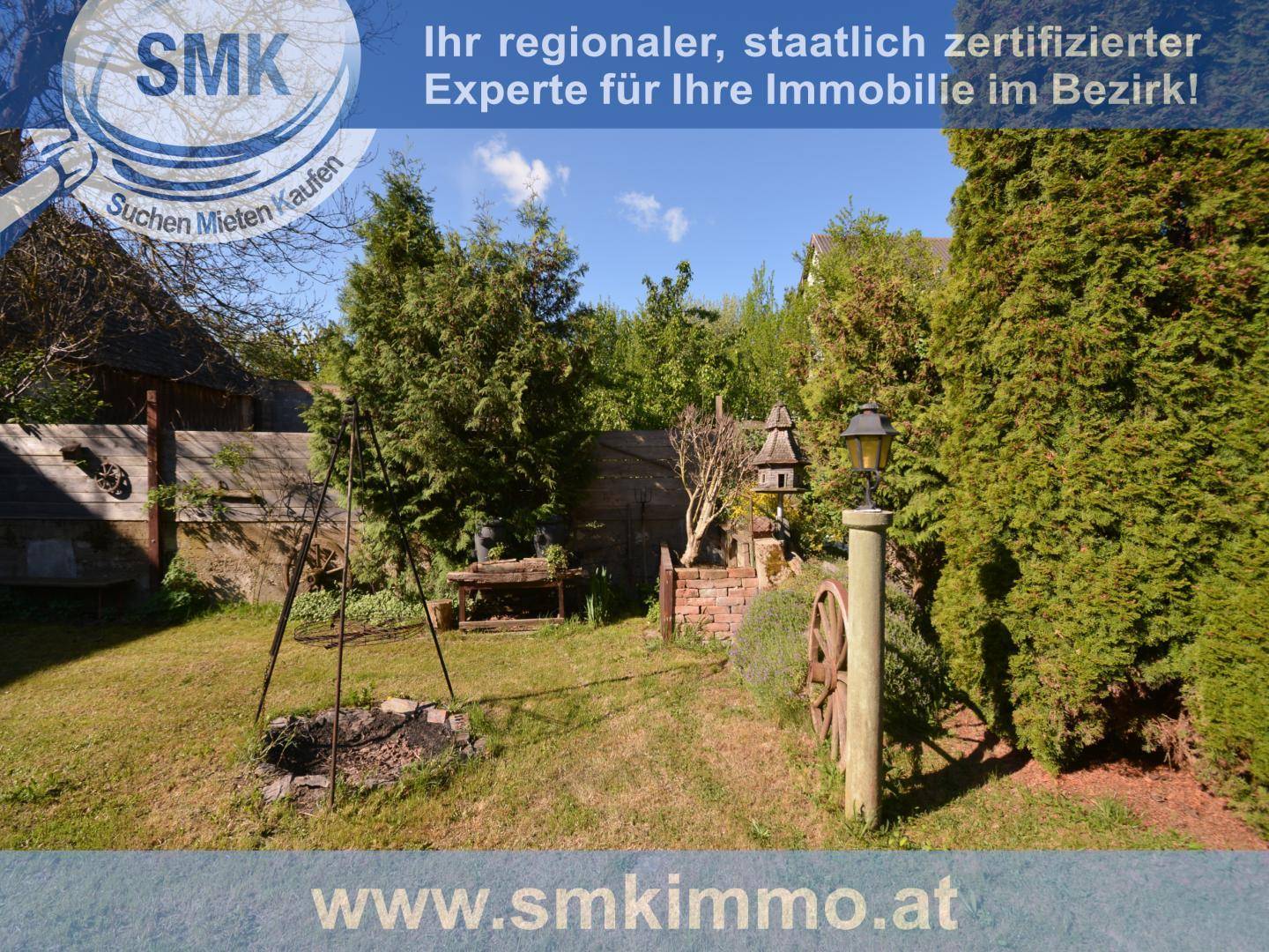 Gartenbereich mit Feuerstelle, Laterne und dekorativen Elementen in ländlicher Umgebung.