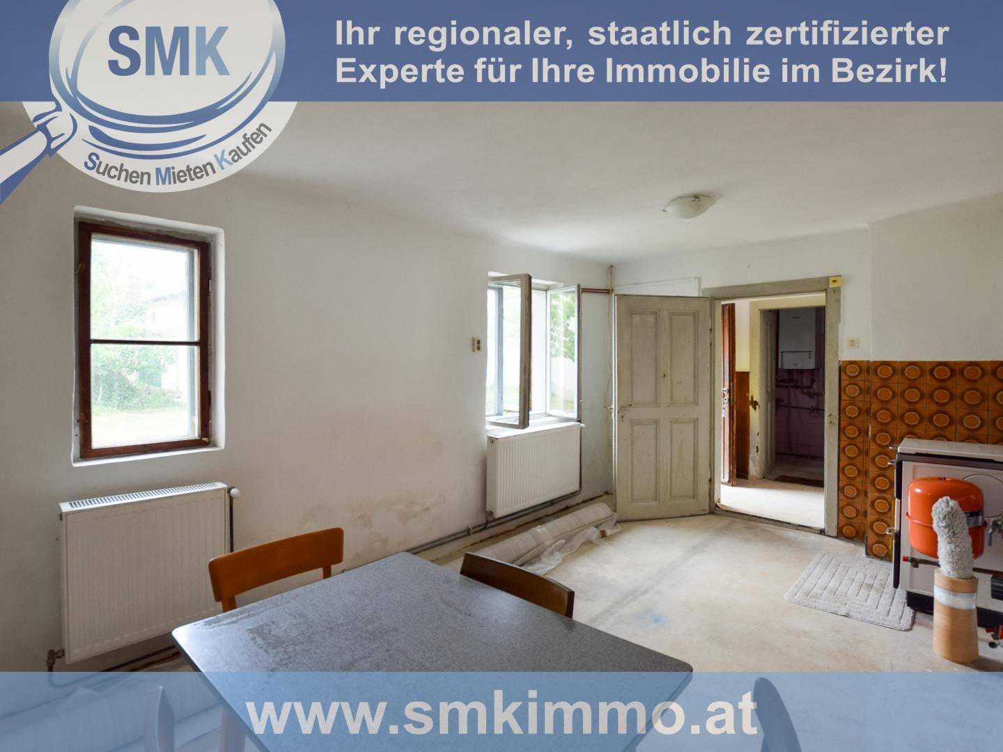 Einfache Küche oder Essbereich mit Tisch, Stühlen und gemusterten Wandfliesen an der Seite.