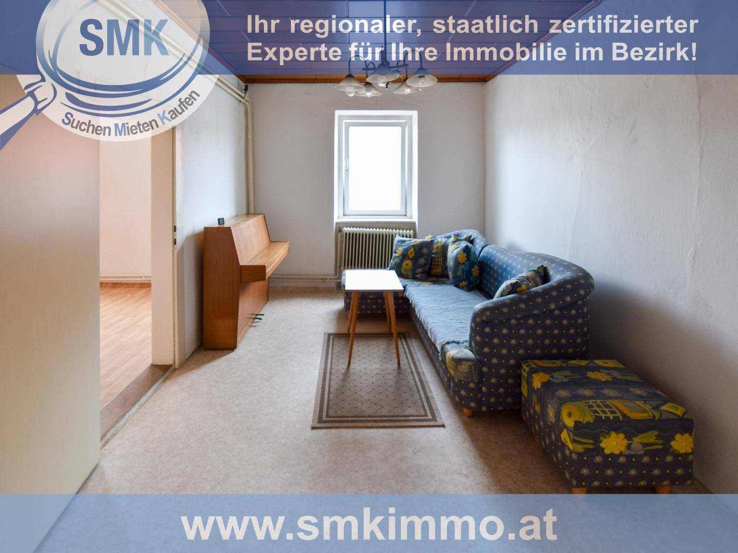 Gemütliches Wohnzimmer mit gemustertem Sofa, kleinem Tisch und Fenster mit Heizkörper.