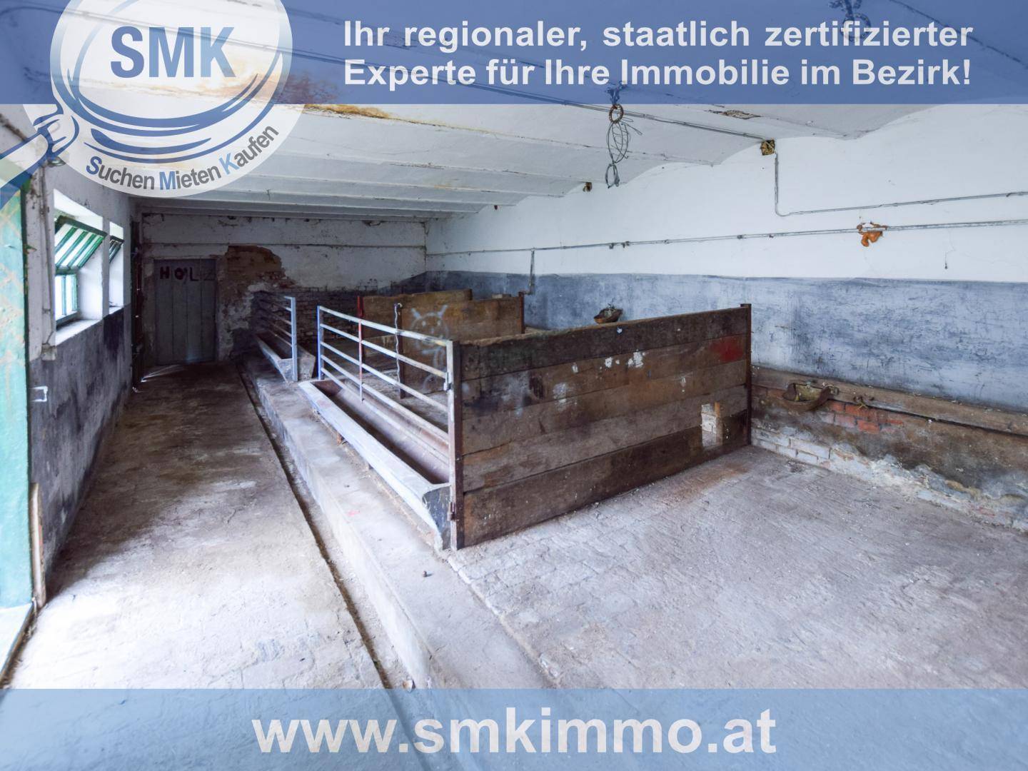 Alter Stall oder Scheune mit Holztrennwänden und Betonboden, in rustikalem Zustand.