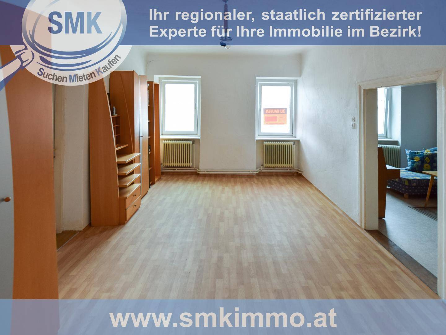 Helles Zimmer mit Laminatboden, zwei Fenstern, Heizkörpern und eingebauten Holzschränken.