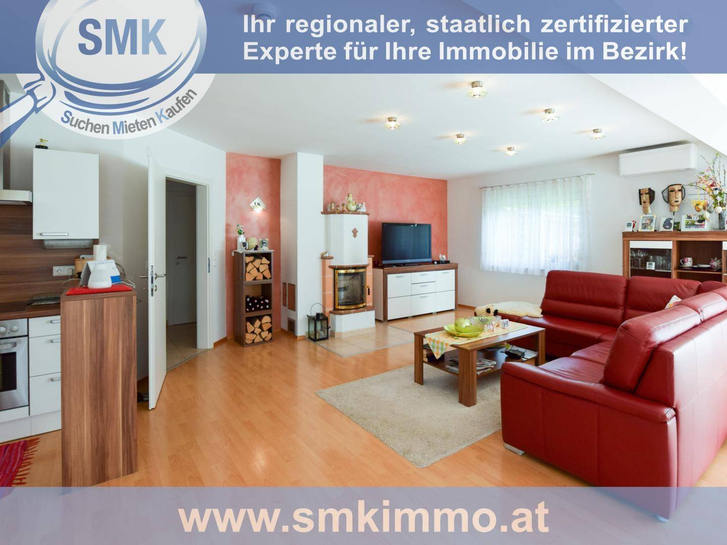Heller Wohnbereich mit rotem Sofa, Kachelofen und offener Verbindung zur Küche.