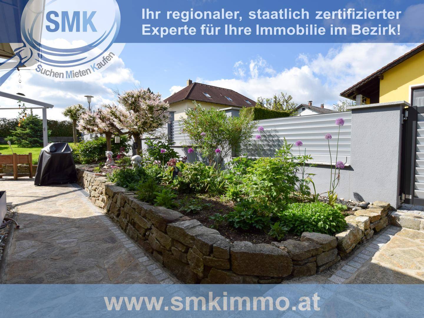 Gepflegter Gartenbereich mit Steinmauern, Blumenbeeten und blühenden Sträuchern.