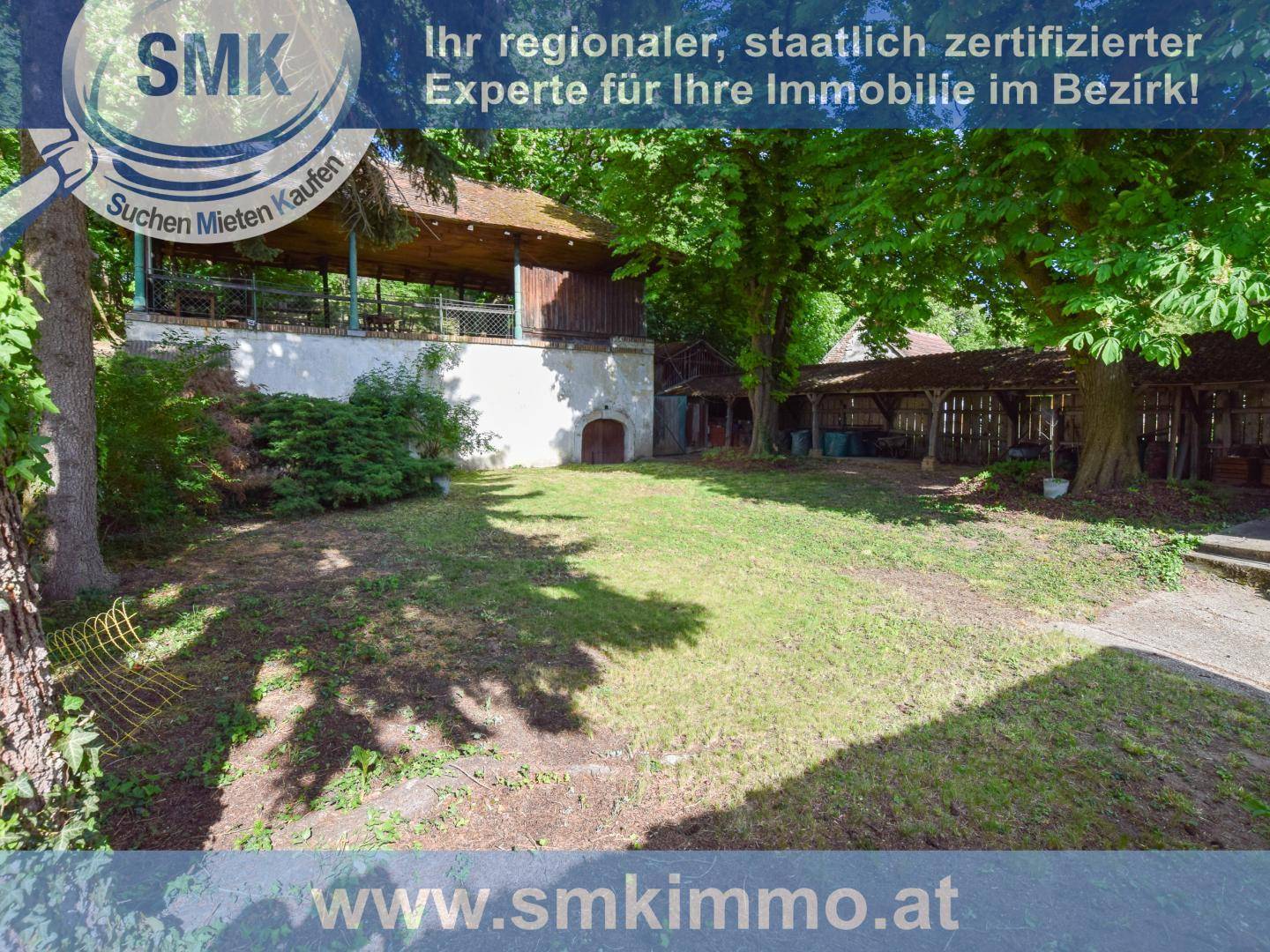 Großer Garten mit Rasenfläche und altem Baumbestand, im Hintergrund ein überdachter Bereich.