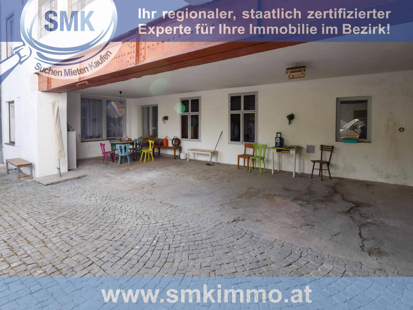 Überdachter Außenbereich mit gepflastertem Boden und bunten Stühlen, ideal für geselliges Beisammensein.
