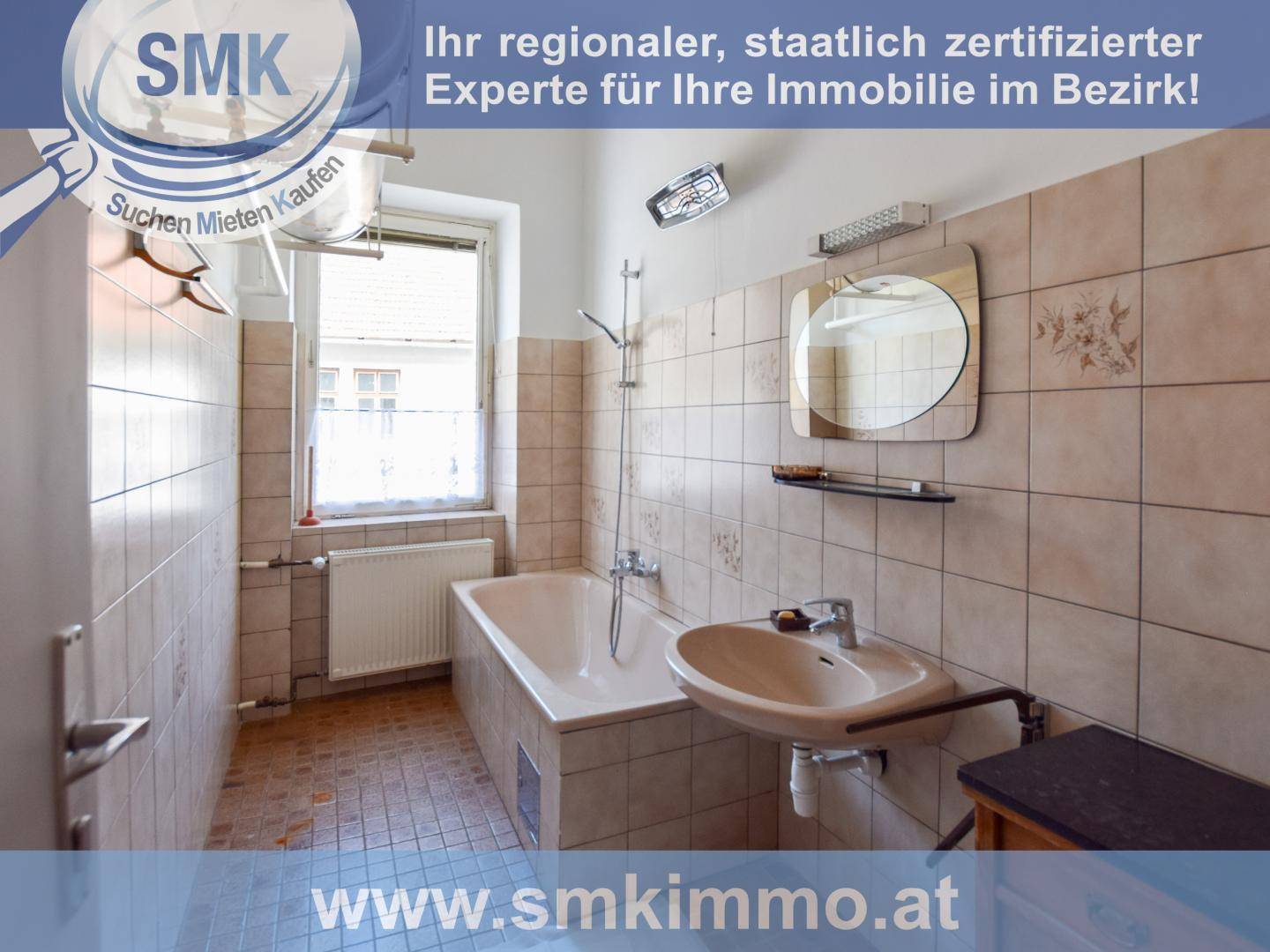 Badezimmer mit Badewanne, Waschbecken und Fliesen an den Wänden, in älterem Zustand.