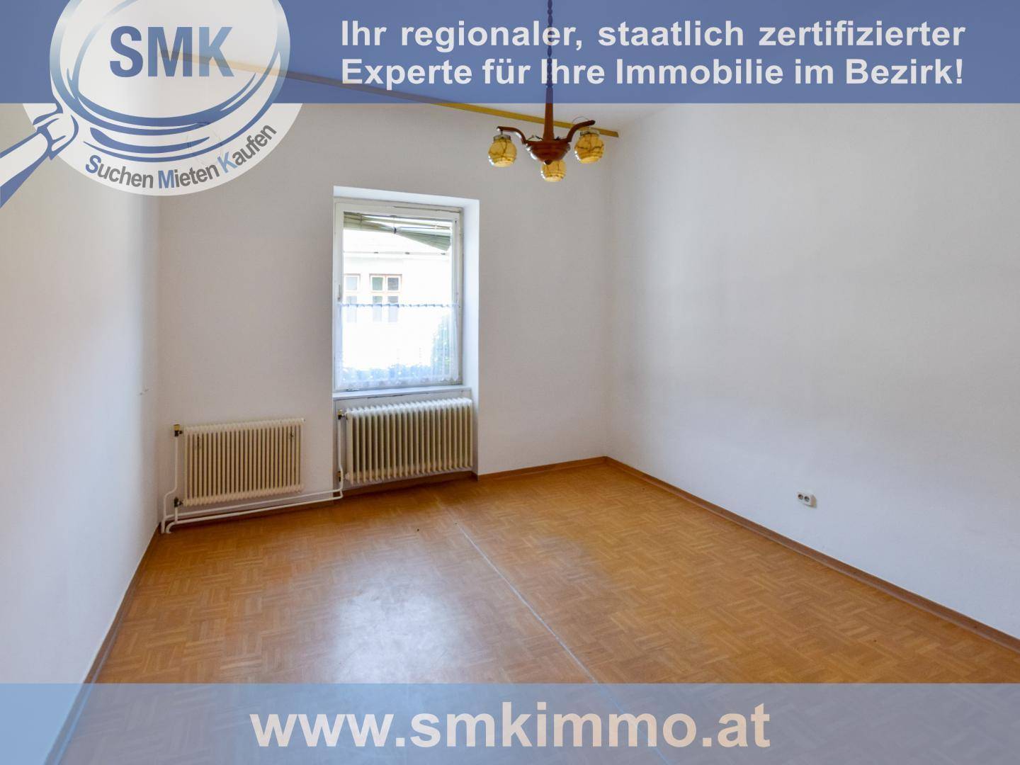 Leeres Zimmer mit Fischgrätparkett und einem Fenster, das auf die Straße blickt.