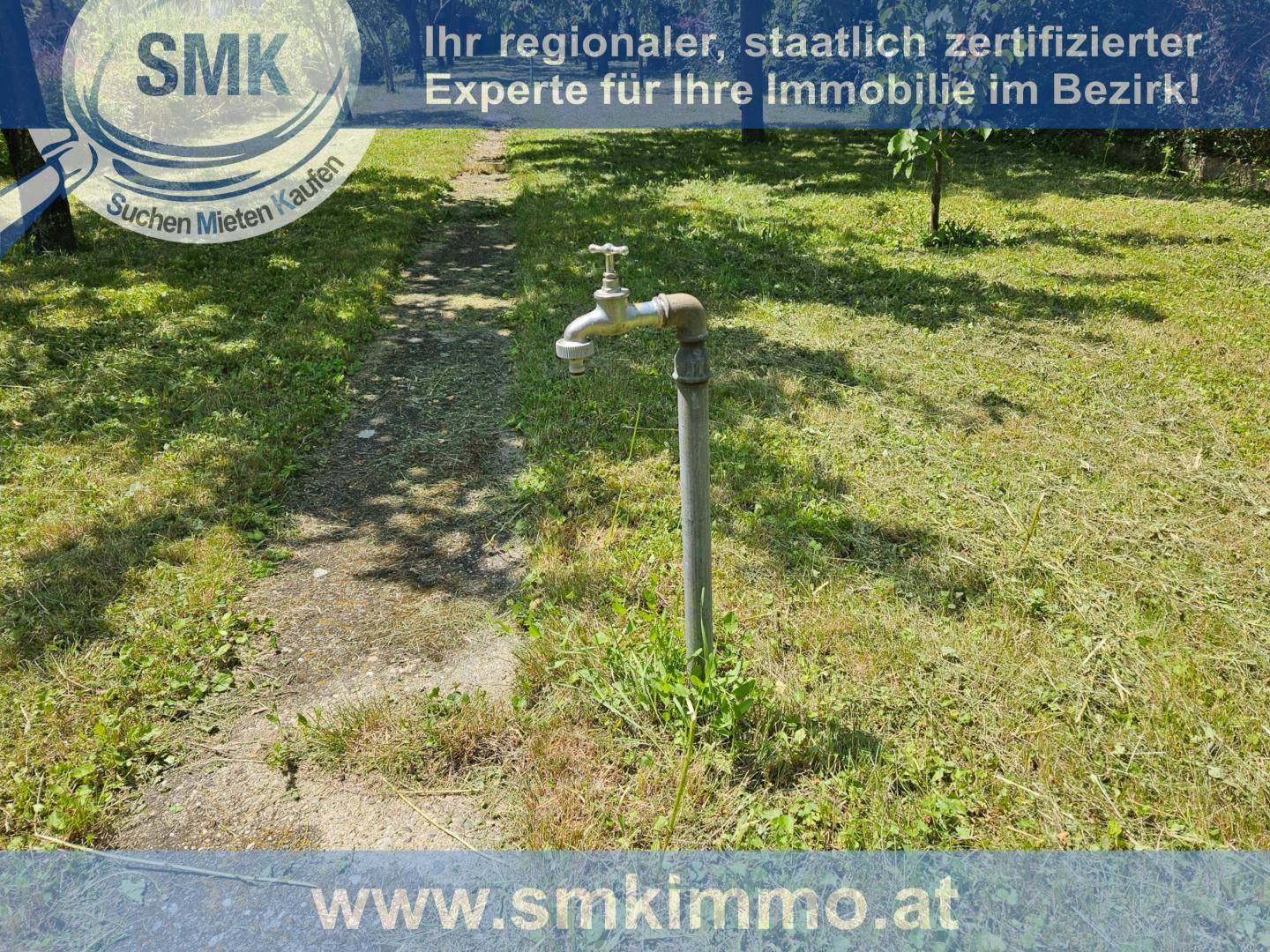Außenwasserhahn auf einem Pfosten im grünen Gartenbereich, bereit zur Bewässerung.
