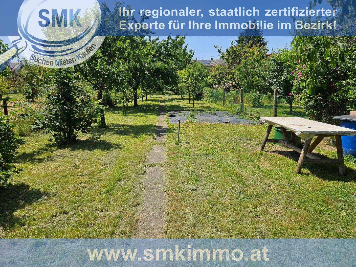 Gartenbereich mit einem einfachen Holztisch und einem Pfad, umgeben von Bäumen und Gras.