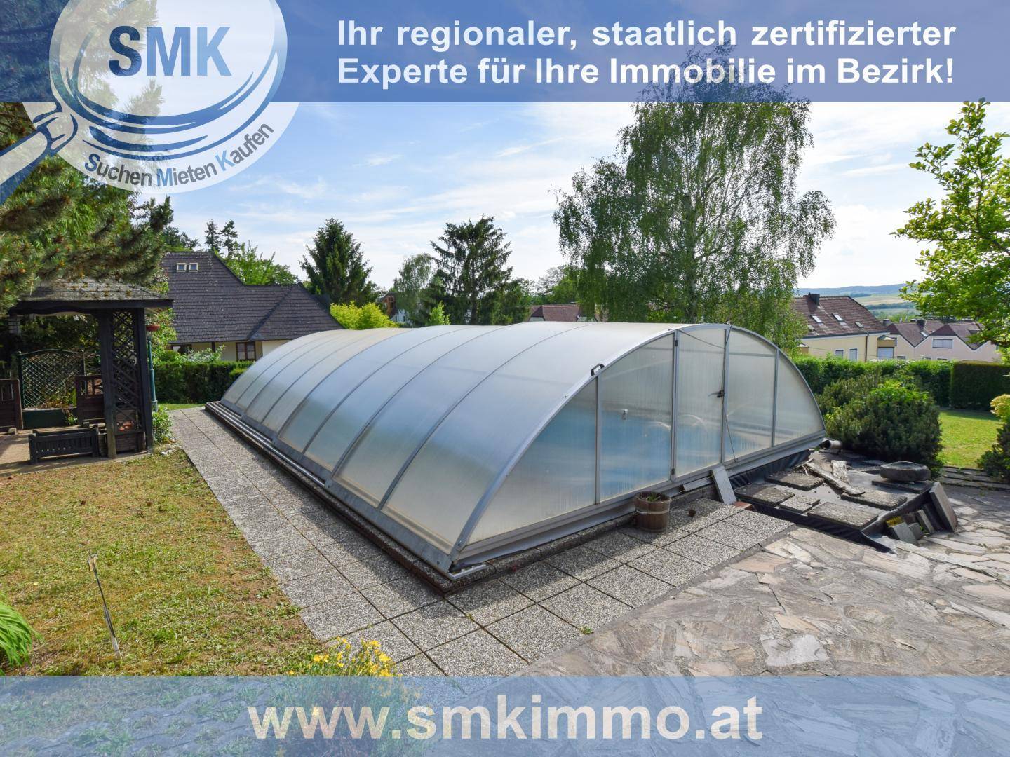 Überdachter Swimmingpool im Gartenbereich, umgeben von Bäumen und Grünflächen.