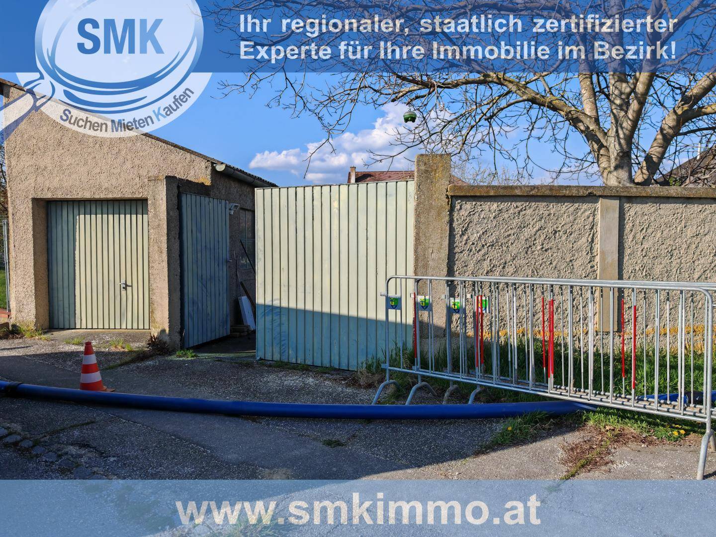 Außenansicht einer Garage mit zwei Toren und einem Holztor, umgeben von einer Betonmauer und Grünflächen.