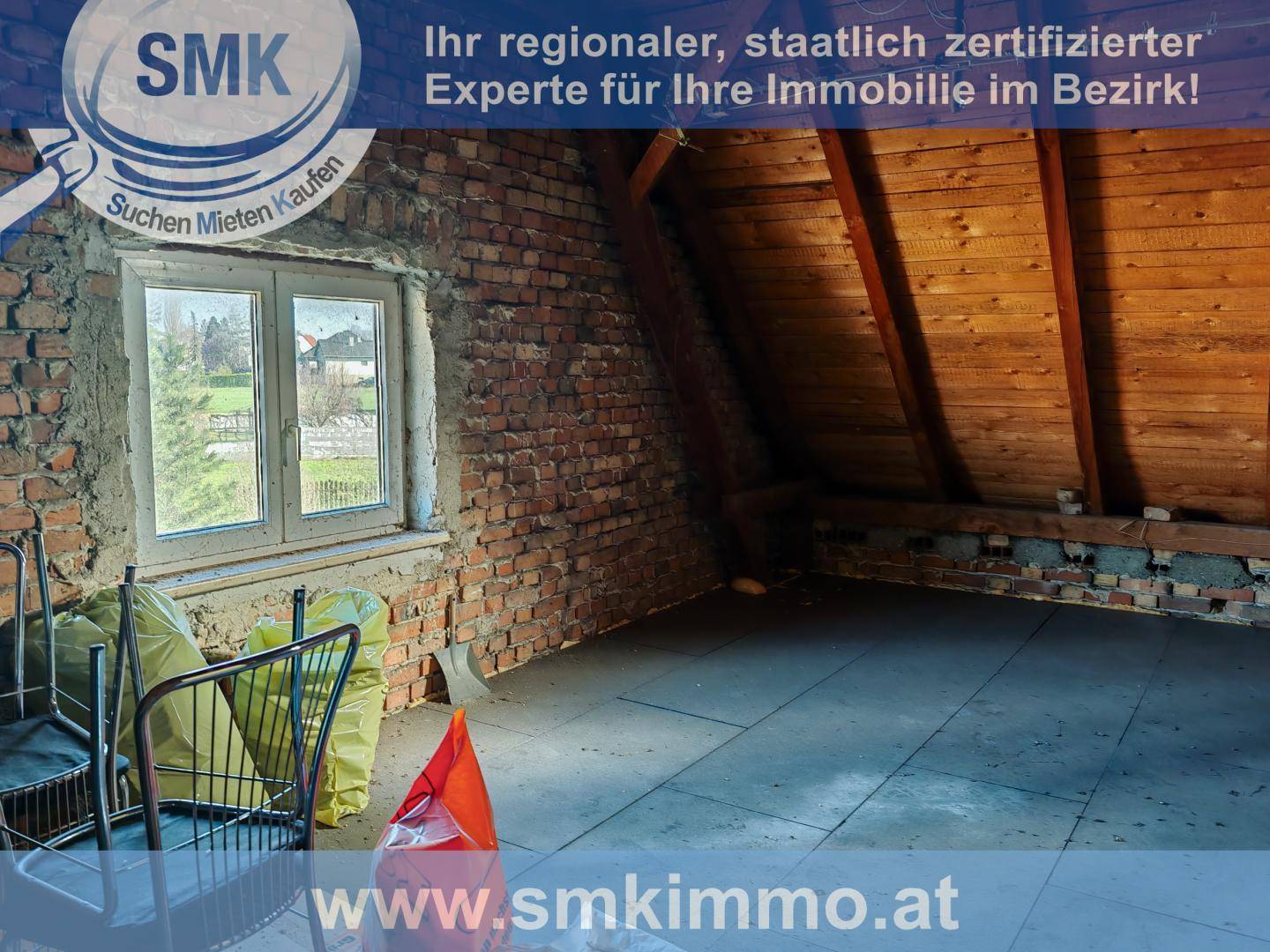 Dachbodenraum mit freiliegenden Ziegelwänden, Holzbalken und einem Fenster, unfertiger Zustand.