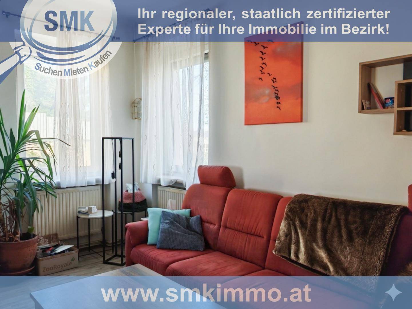 Gemütliches Wohnzimmer mit rotem Sofa, Pflanzen und einem Fenster mit Vorhängen.