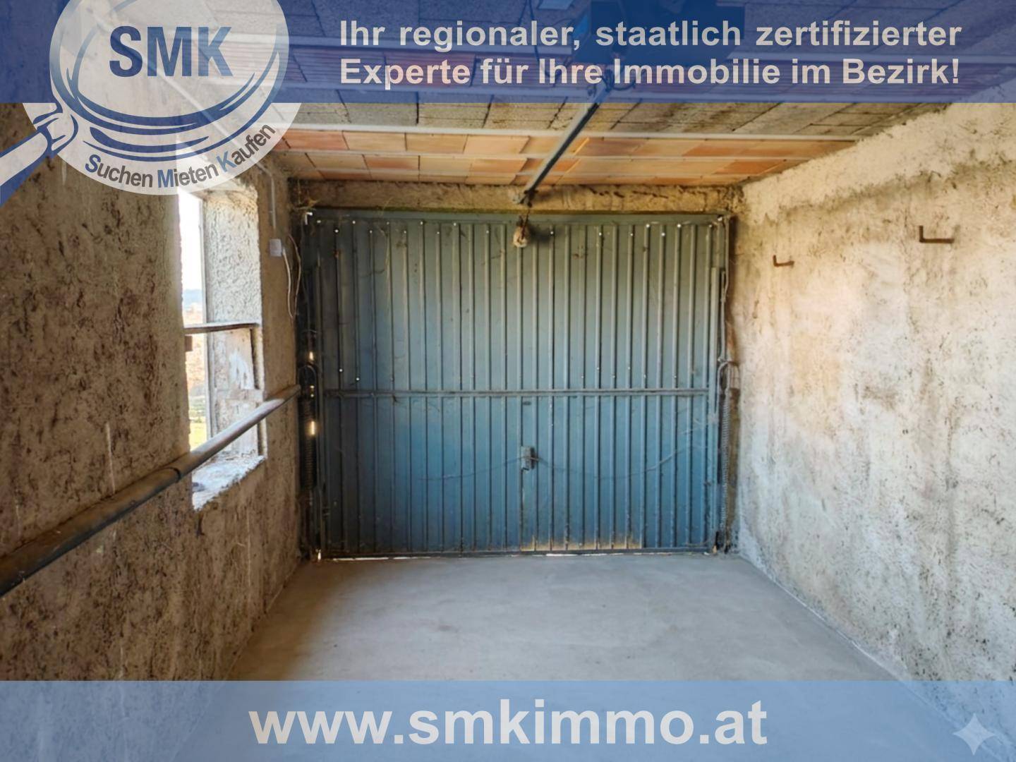 Innenansicht einer einfachen Garage mit großem Metalltor, rauen Wänden und Betonboden.