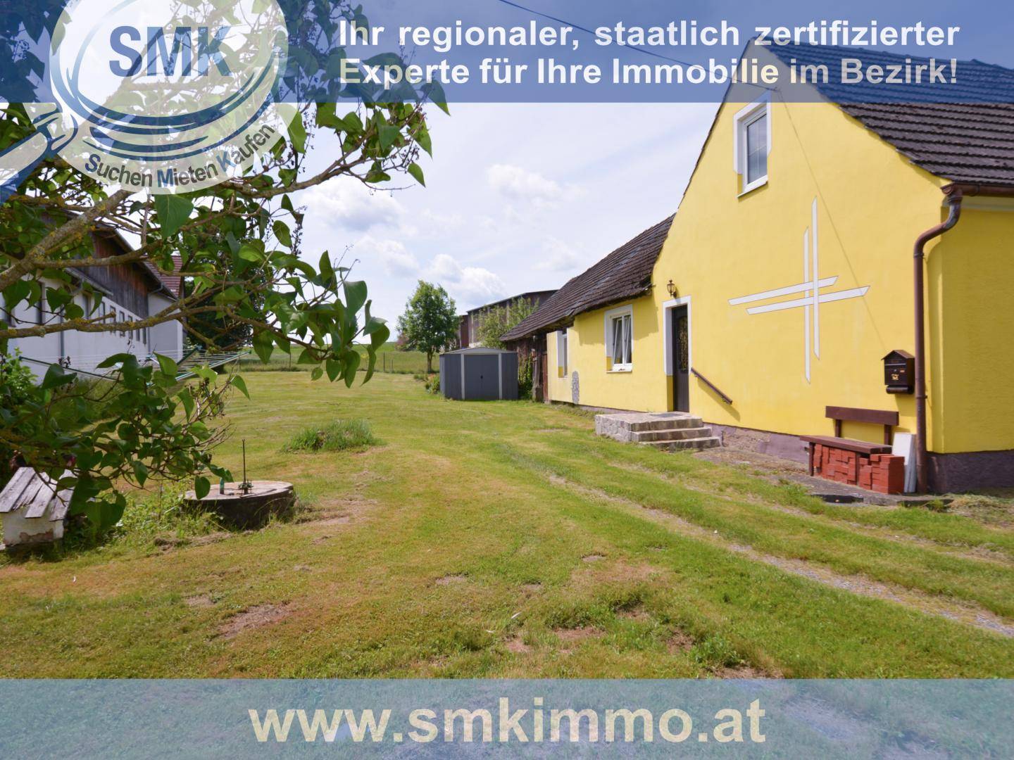 Gelbes Einfamilienhaus mit großem Garten und Nebengebäude unter blauem Himmel.