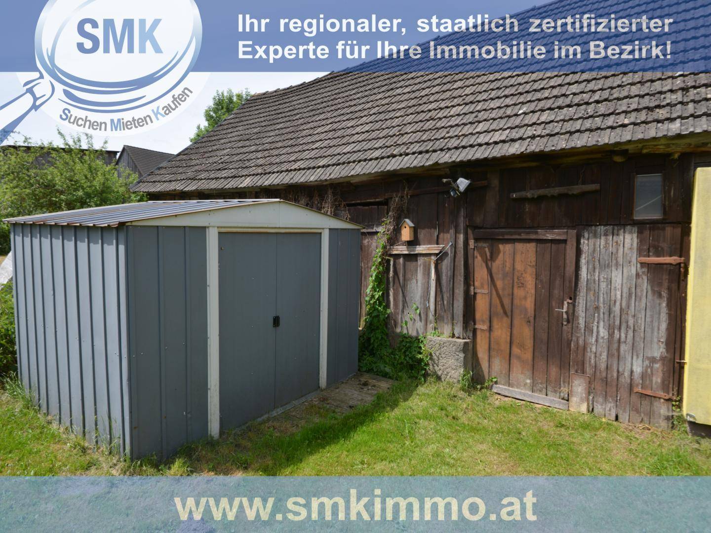 Grauer Metallschuppen neben einem alten Holzgebäude im Gartenbereich, bietet zusätzlichen Stauraum.