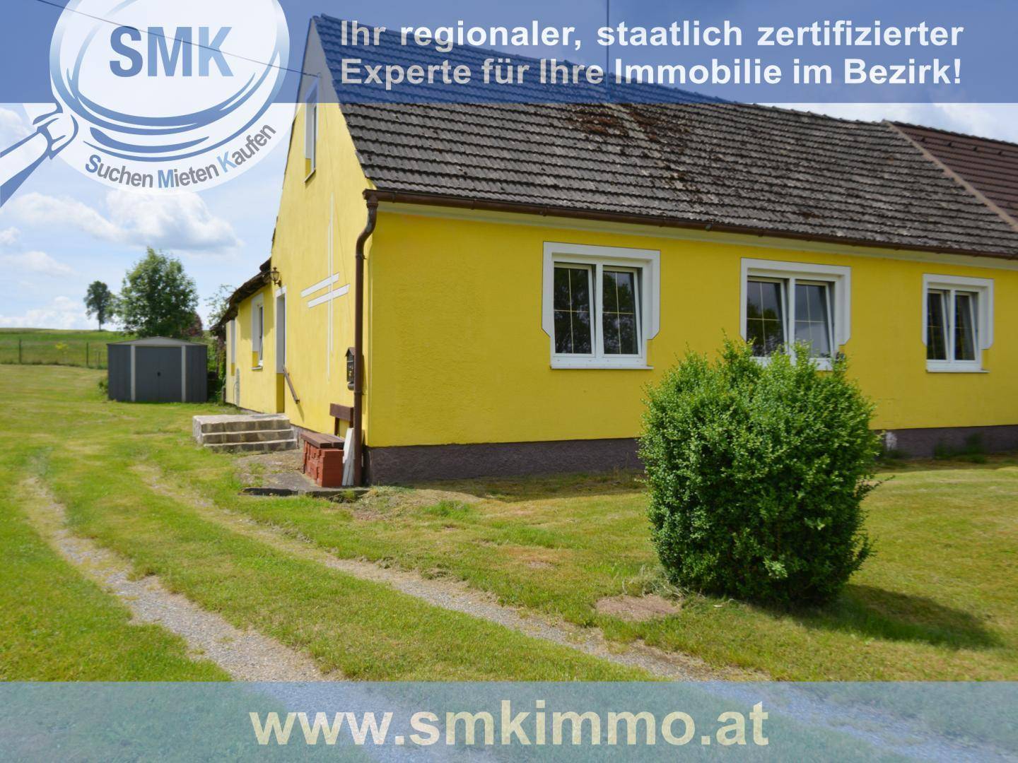 Gelbes Haus mit weiß gerahmten Fenstern und einem grünen Busch im Vorgartenbereich.