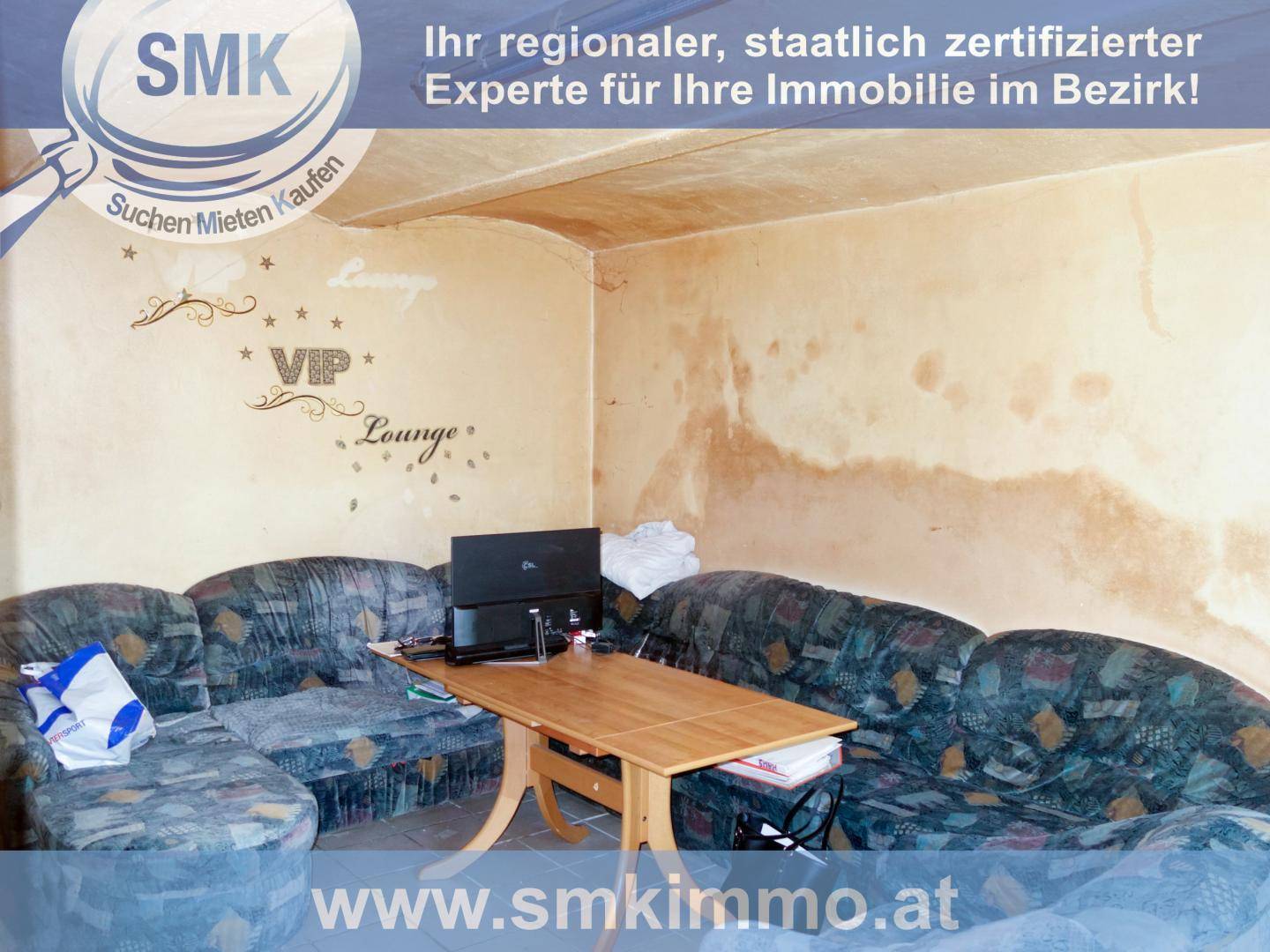 Wohnzimmer mit älteren Sofas und Holztisch, Wanddekoration und sichtbaren Gebrauchsspuren.