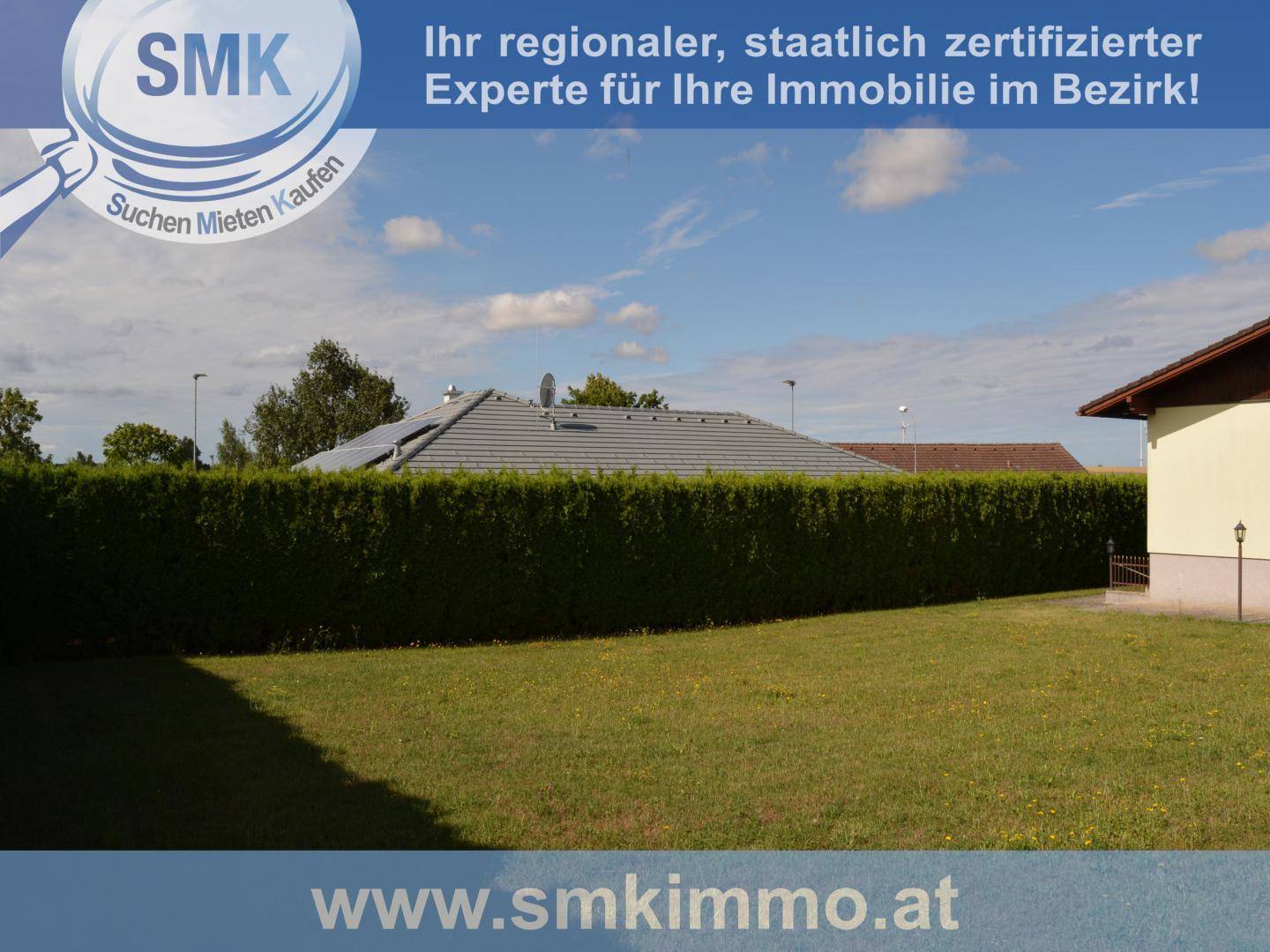 Weitläufige Rasenfläche des Gartens, begrenzt von einer hohen Hecke und Blick auf ein Nachbardach.