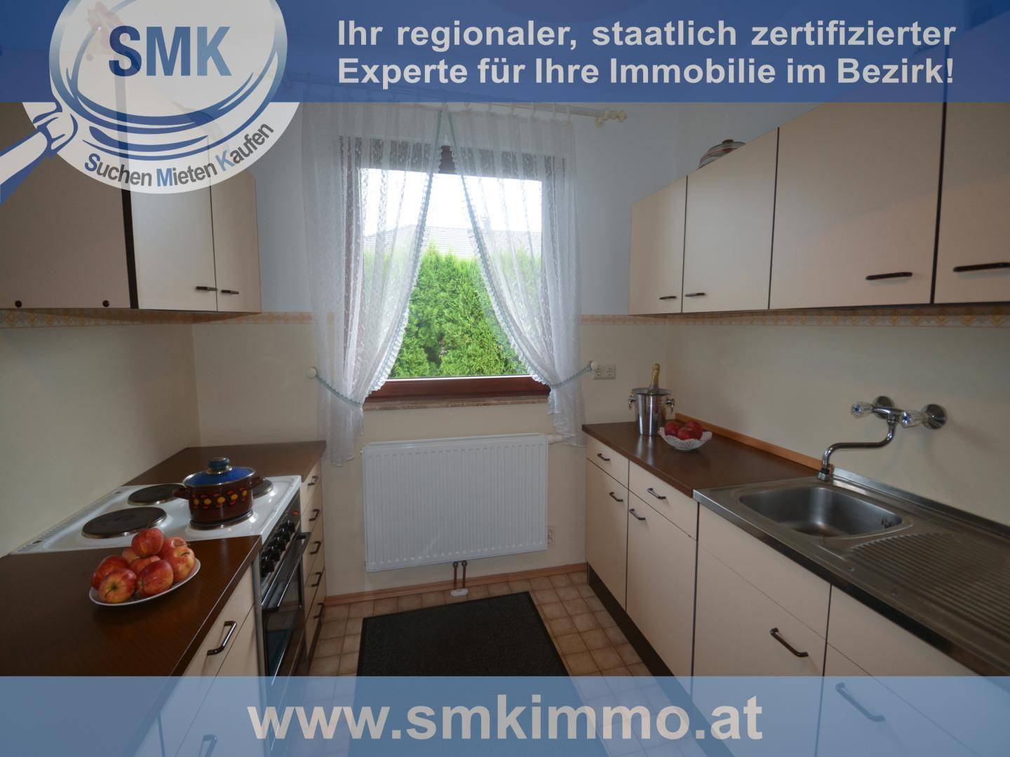 Küche mit Einbauschränken, Herd und Spüle, sowie einem Fenster mit Blick ins Grüne.