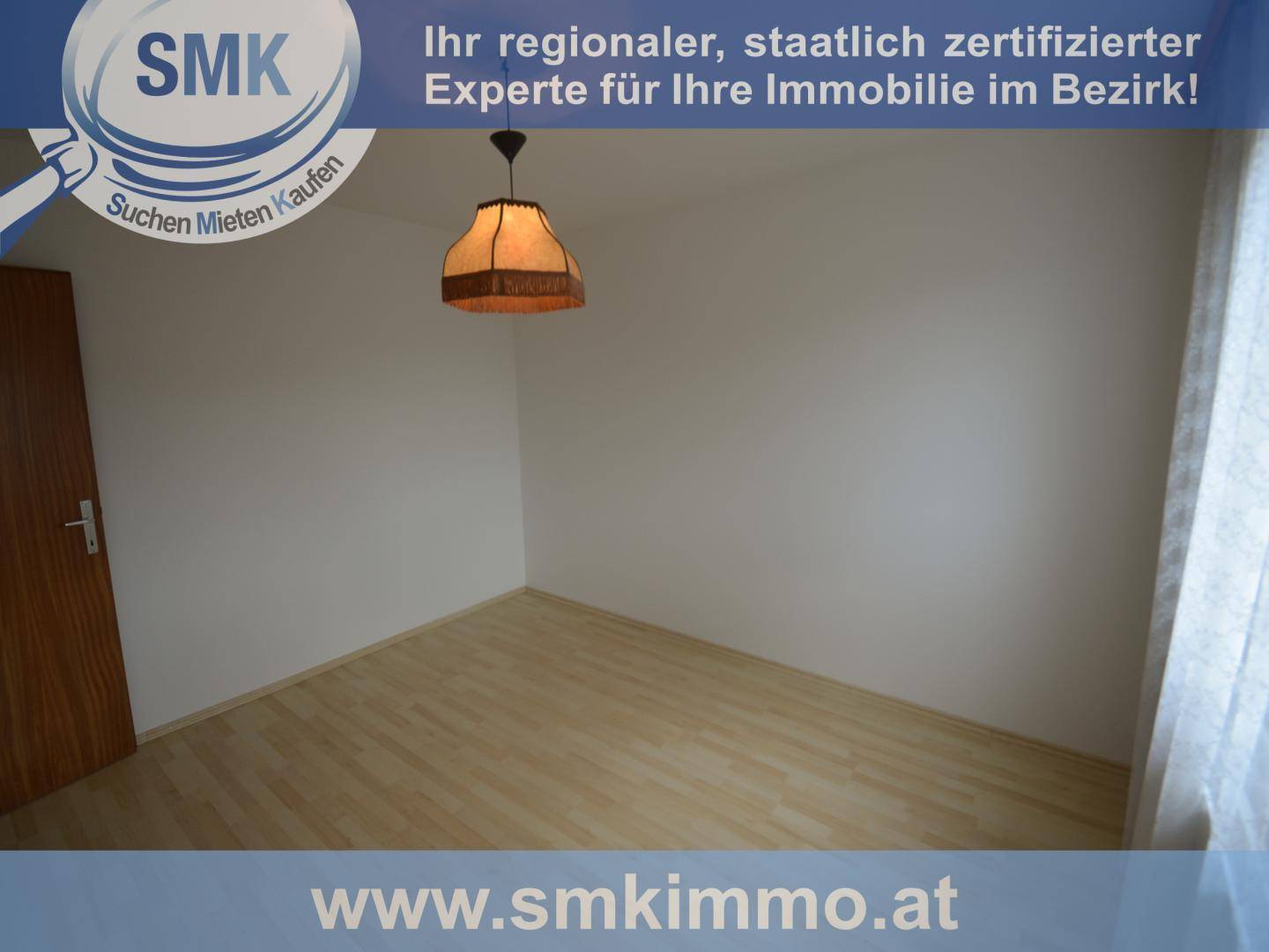 Leerer Raum mit hellem Laminatboden und einem Fenster, das viel Tageslicht hereinlässt.