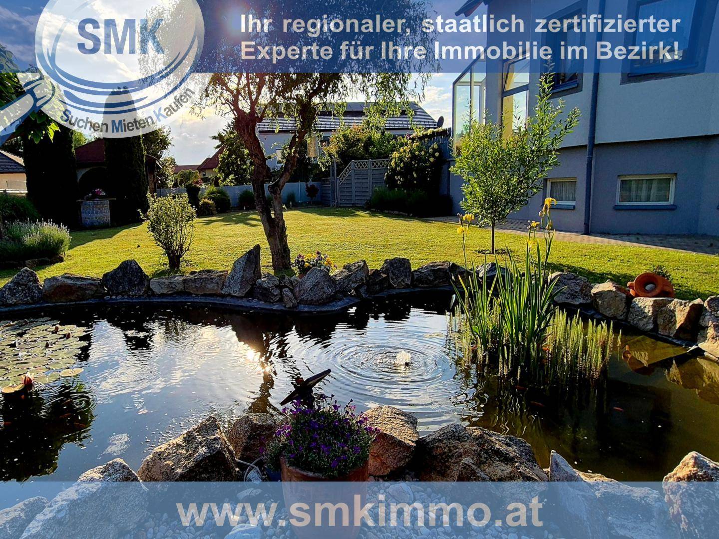 Gepflegter Garten mit einem dekorativen Teich und Wasserspiel, umgeben von Grünflächen und einem Wohnhaus.